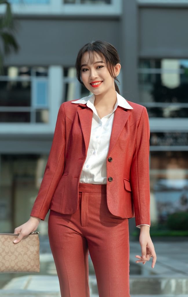 Smiling Asian businesswoman in stylish red suit standing outdoors, conveying confidence and professionalism.